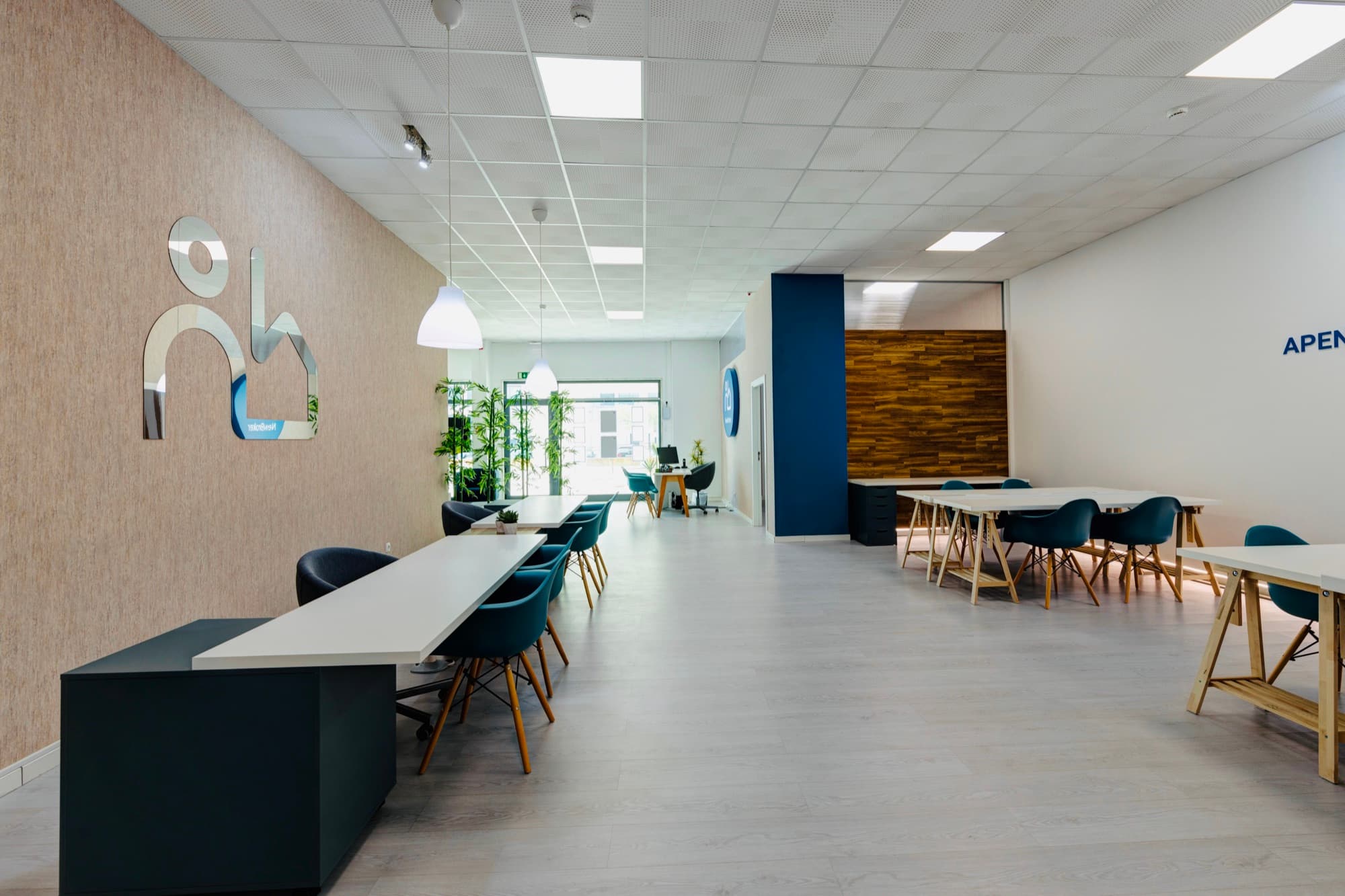 Interior da agência NewBroker: mesas de trabalho e a marca em relevo na parede